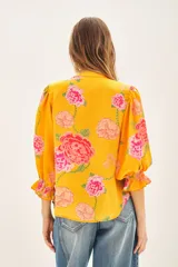 Camisa color naranja con estampado de flores rosas, escote redondo, mangas al codo terminadas con elástico y volado. Confeccionada en viscosa estampada.