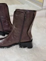 Botas cortas color chocolate con textura de cocodrilo, punta cuadrada y tacón bajo. Cuentan con cierre lateral.