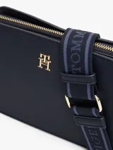 Bandolera Tommy Hilfiger color azul marino, de forma rectangular con logo dorado en el frente y correa de tela con inscripción de la marca.