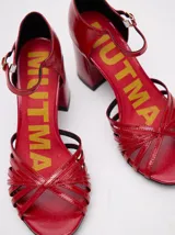 Sandalias negras de charol con tiras cruzadas en el empeine, pulsera con hebilla al tobillo y tacón cuadrado.