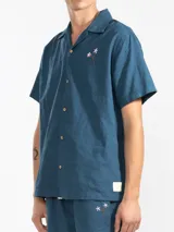 Camisa azul de hombre de calce relajado y corte cuadrado, confeccionada en una mezcla liviana de lino y algodón. Presenta cuello tipo camp, cierre con botones de madera grabados con el logo y un bordado sutil en el pecho izquierdo con forma de palmera. Incluye patch con logo de la marca.