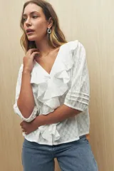 Blusa color crema con diseño calado, escote en V y volados frontales. Tiene mangas 3/4 con puños elastizados y cierre frontal con botones.