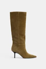 Bota de caña alta color verde oliva, confeccionada en serraje, con pespuntes decorativos y tacón tipo kitten. Acabado en punta.