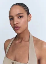 Chaleco de vestir color beige, con cuello halter y escote cuadrado, cierre frontal de botones y bolsillos de solapa.