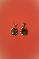 Aros colgantes dorados con forma irregular, engastados con una piedra o resina de color marrón oscuro y verde azulado veteado. El poste superior tiene un diseño orgánico y texturizado.