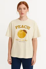 Remera color crema con estampado de durazno, texto "Peach" y la frase "Have a nice day! Please recycle".