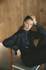 Camisa corta de denim celeste, con cuello solapa, manga larga, bolsillo delantero de plastrón y cierre frontal con botones metálicos.