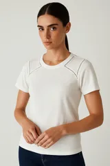 Remera blanca de algodón, corte holgado, con cuello redondo y detalle de calado en los hombros.