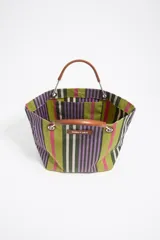 Bolso tote de tela a rayas verticales en tonos verde oliva, lila, blanco y rosa. Tiene doble asa de mano de cuero marrón y logo de la marca en etiqueta de cuero.