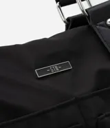 Cartera satchel mediana de PU color negro, con textura capitoneada, doble asa corta y correa larga extraíble. Posee cierre principal con cremallera y bolsillos externos con cremallera.