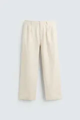 Pantalón de corte recto, color beige claro, con pliegues frontales y bolsillos de vivo en la parte trasera.