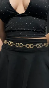 Cinturón dorado tipo caderín con cadena de eslabones y dijes con el logo de la marca.