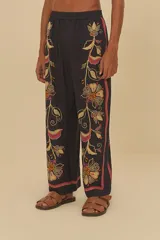 Pantalón negro con estampado floral en tonos naranja, amarillo y rojo. Corte holgado, cintura elástica de tiro medio y largo amplio.