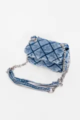 Bandolera azul de denim con diseño acolchado en forma de rombos. Tiene correa de cadena metálica y asa corta de denim.