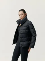 Campera puffer negra ultraligera con cuello alto, cierre de botones a presión, bolsillos laterales y mangas acampanadas. Relleno vegano.