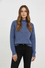 Polera de tejido acrílico azul, de corte holgado, con cuello tipo polera (mock neck) y mangas largas.