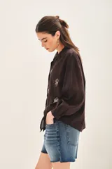 Camisa blanca de voilé de algodón con escote redondo y bordados de ojos en el delantero. De corte recto y mangas largas con puños abotonados.