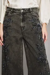 Pantalón de denim de corte ancho y tiro alto, color negro lavado, con apliques bordados florales en tonos oscuros a lo largo de las piernas.