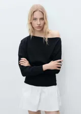 Vestido corto negro con falda blanca, de corte ajustado, con cuello asimétrico y manga larga.