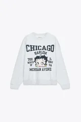 Sudadera gris melange de cuello redondo y manga larga con puños elásticos. Estampado frontal con texto "Chicago Harlem" y dibujo de Betty Boop.