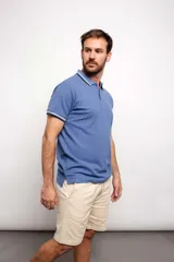 Chomba celeste con cuello y mangas con detalles de líneas blancas y azul marino. Corte clásico, mangas cortas y cuello polo con botones.
