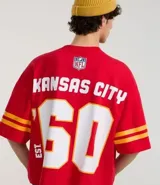Remera roja de algodón con estampado del logo de los Kansas City Chiefs, el nombre del equipo y el número 60 en blanco. Tiene mangas cortas con rayas amarillas y rojas.