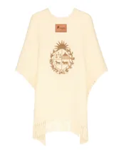 Ruana de lana merino color crudo, con flecos en el ruedo y escudo nacional bordado en el frente.