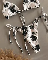 Conjunto de bikini blanco con estampado de flores negras. El corpiño es triangular con tirantes regulables y la bombacha es regulable con tiras en los costados, pudiendo usarse como vedetina o colaless.