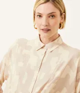 Camisa de crepé color beige con estampado geométrico en tonos neutros, cuello camisero, manga larga y cierre con botones. Tiene un lazo frontal para atar.