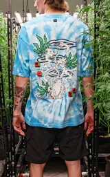 Remera celeste con efecto tie-dye, corte extra oversize, hombros caídos y cuello redondo. Estampa pequeña en el pecho con un personaje fumando sobre una hoja de marihuana.