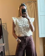 Top sin mangas color crudo, tejido en crochet con motivos circulares florales. Presenta cuello alto y pequeños volados en los hombros.