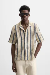 Camisa de crochet color beige con rayas verticales azules, cuello bowling, manga corta y cierre frontal con botones.