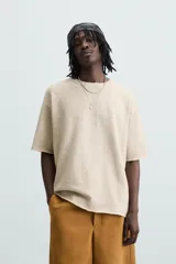 Camiseta color beige de punto tejido en hilatura de algodón, corte relaxed fit, cuello redondo y manga corta. Estampación con efecto lavado combinada a contraste en espalda. Acabados irregulares.