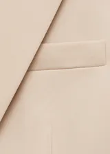 Blazer color beige con solapas de muesca, cierre frontal con un botón, hombros estructurados, corte entallado, forro interior y dos bolsillos de ribete en la parte delantera.