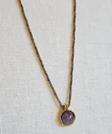 Collar con cadena de eslabones dorados y dije redondo con piedra amatista engarzada en metal dorado.