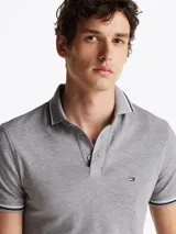Chomba gris de algodón elástico con cuello y mangas ribeteadas en blanco y negro. Tiene cartera de tres botones, logo de Tommy Hilfiger bordado en el pecho y corte slim.