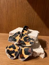 Llavero con forma de trébol de cuatro hojas, confeccionado en cuero con estampado de leopardo. Incluye una tira de sujeción con un broche metálico y un dije plateado con la inscripción "G. Shaw".