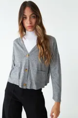 Cardigan tejido gris con escote en V, cierre con botones de madera, bolsillos tipo parche y logo en grifa de cuero.