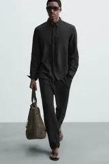 Pantalón negro de corte regular fit, con bolsillos laterales y bolsillos traseros de vivo. Presenta un bajo con vuelta y cierre frontal con cremallera y botón.