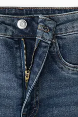 Jean de denim azul con tiro alto, cierre con botón y piernas amplias con bajos acampanados.