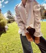 Camisa marrón de algodón con cuello clásico, cierre frontal con botones dorados y mangas largas abullonadas con puños elásticos.