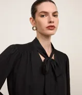 Blusa negra de crepé con cuello con lazo, mangas largas y pliegues en los hombros.