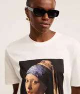 Remera de algodón color blanco, con cuello redondo y mangas cortas. Estampa frontal con la pintura "La joven de la perla" de Johannes Vermeer.