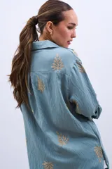 Camisa celeste con bordado de hojas color dorado, de corte holgado y manga larga con puños abotonados.