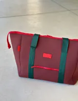 Bolso de neopreno color burdeos con cierre rojo, incluye monedero y varios compartimentos internos y externos.