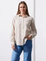 Camisa color beige de lino, marca Dash. Tiene cuello con solapa, abertura central con botones, bolsillo aplicado en el pecho y mangas largas regulables con presilla y botón.