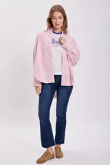 Camisa oversize a rayas verticales rojas y blancas, con cuello clásico, cierre frontal con botones y mangas largas con puños abotonados.