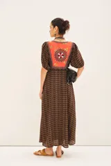 Vestido largo de viscosa con estampado geométrico en tonos marrón y naranja. Presenta escote en V con un panel bordado en la zona del busto en tonos naranja, rojo y blanco. Tiene mangas cortas abullonadas y cintura marcada con elástico.
