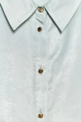 Camisa celeste de tejido satinado, con cuello solapa, manga larga con puños y cierre frontal con botones.