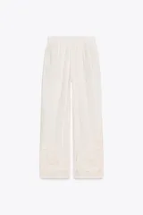 Pantalón de tiro medio color crudo, confeccionado en mezcla de algodón y lino, con cintura elástica ajustable con cordones, bolsillos laterales ocultos y detalle de bordados perforados a tono en el ruedo.
